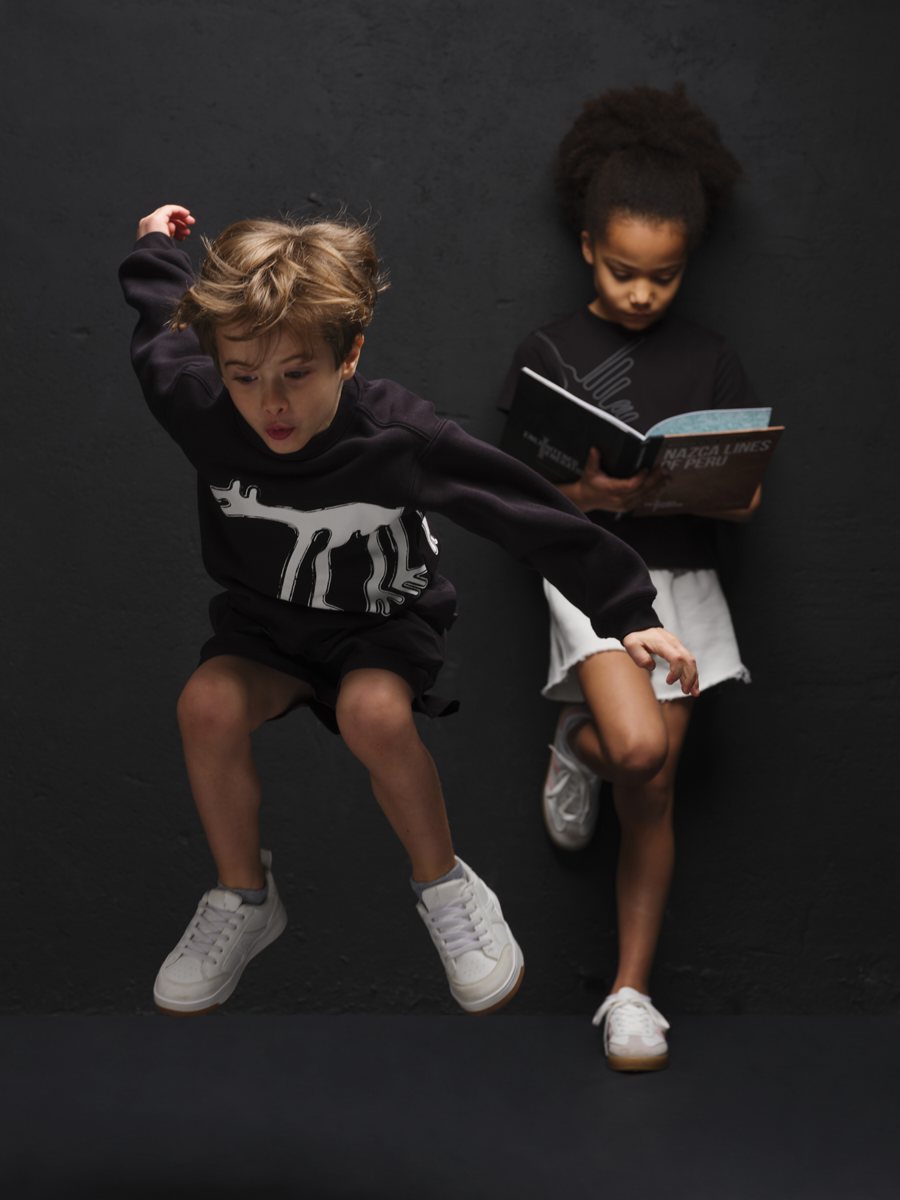A boy jumping in front of a dark wall while a girl leans back reading a book