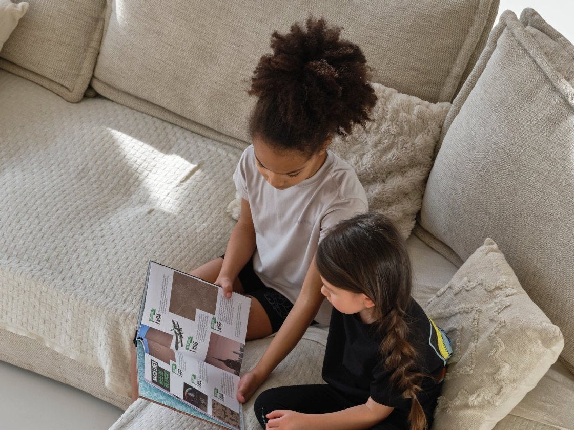Two girls on a big cream sofa, reading an Enlightened Generation book together