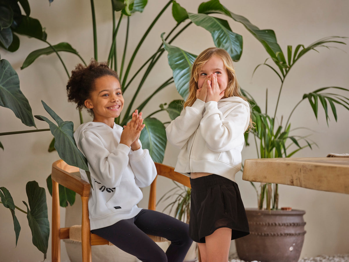 Two girls laughing together by a big green plant