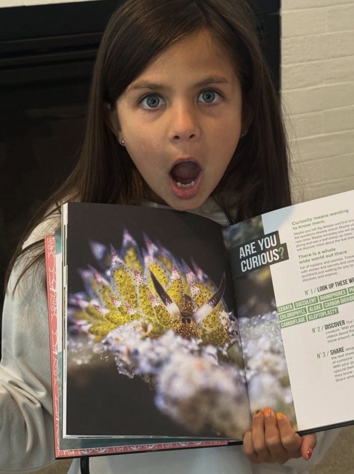 A girl holding the Leaf Sheep of the Sea book open, mouth wide open in surprise